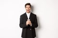 Portrait of happy good-looking man, wearing black suit, laughing from happiness and using mobile phone, standing over Royalty Free Stock Photo