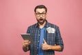 Portrait of happy handsome bearded young hipster man in checkered shirt standing, holding tablet computer and money. Indoor, Royalty Free Stock Photo