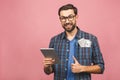 Portrait of happy handsome bearded young hipster man in checkered shirt standing, holding tablet computer and money. Indoor, Royalty Free Stock Photo