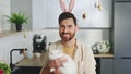 Portrait of the happy handsome man holding the fluffy easter rabbit, wearing bunny ears. Smiling male is getting ready