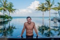 Portrait of happy handsome man model sitting at the edge of the swimming pool at the tropical island luxury resort Royalty Free Stock Photo