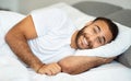 Portrait of happy handsome millennial man lying on bed