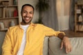 Portrait of happy handsome young black guy smiling, sitting on sofa, relaxing at home, free space Royalty Free Stock Photo