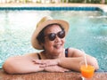 Happy and healthy Asian senior  woman wearing straw hat and sunglasses  drinking  orange juice  in the swimming pool, smiling and Royalty Free Stock Photo