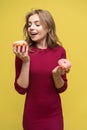 Portrait of happy hipster girl choosing beetwen two donutes. Studio portrait over yellow background.