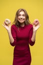 Portrait of happy hipster girl choosing beetwen two donutes. Studio portrait over yellow background.