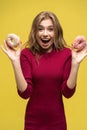 Portrait of happy hipster girl choosing beetwen two donutes. Studio portrait over yellow background.