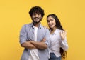 Portrait of happy indian couple embracing, woman showing okay gesture and smiling at camera over yellow background