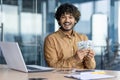 Portrait of a happy Indian man sitting in the office at a desk with a laptop and holding cash money in his hands Royalty Free Stock Photo