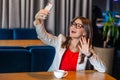 Portrait of happy joyful beautiful stylish brunette young woman in glasses sitting on video call or doing selfie with toothy smile Royalty Free Stock Photo