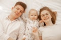 Portrait of happy joyful merry couple, newborn child, lying on white bed in blanket. Mother, father. Bound family goals