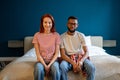 Portrait of happy married interracial diverse couple smiling at camera while sitting together on bed Royalty Free Stock Photo