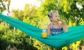 Portrait of happy kid cute girl is eating pizza and drink orange juice from jar with straw sitting on green hammock on Royalty Free Stock Photo