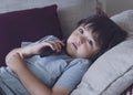 Portrait of happy kid lying on sofa watching TV, Positive child boy holding remote control looking up with smilng face. Relaxing,