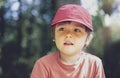 Portrait of happy kid wearing red cap hat sitting in the park with bright light sunny day, Portrait child playing outdoor in