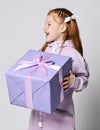 Portrait of happy laughing kid girl in pink jumpsuit with big blue gift box with ribbon and bow in hands looking aside Royalty Free Stock Photo