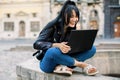 Portrait of a happy laughing young brunette woman, sitting on the city fountain and using laptop computer outdoors Royalty Free Stock Photo