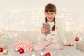 Portrait of happy little adorable girl wearing white casual sweater sitting on bed with cell phone in hands, having video call