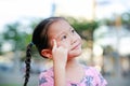 Portrait of happy little Asian child in garden with thinking and looking up. Close-up smiling kid girl with forefinger point on