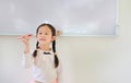 Portrait of happy little Asian child girl or Schoolgirl holding a marker against whiteboard in the classroom. White board with