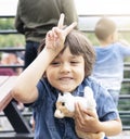 Portrait of happy little boy hugging dog toy and putting fingers on his head and making funny face, Kid having fun playing outdoor Royalty Free Stock Photo