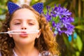 Portrait of a happy little curly girl playing with soap bubbles on a summer nature, wearing a blue ears of tiger Royalty Free Stock Photo