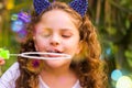 Portrait of a happy little curly girl playing with soap bubbles on a summer nature, wearing a blue ears of tiger Royalty Free Stock Photo