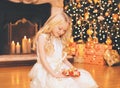 Portrait happy little girl child opens gift box near christmas tree with garland lights and fireplace at home Royalty Free Stock Photo