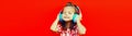 Portrait of happy little girl child in wireless headphones listening to music on red background, blank copy space for advertising Royalty Free Stock Photo
