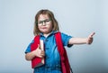 Portrait of happy little girl in glasses hugging a book. Child with backpack laughing and pointing with thumb up Royalty Free Stock Photo