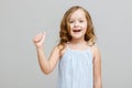 Portrait of a happy little girl on a gray background. A child holds a thumb up. Concept of victory and success