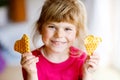 Portrait of happy little preschool girl holding fresh baked heart waffle. Smiling hungry toddler child with sweet