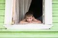 Portrait of happy little smiling boy kid is looking out of rustic wooden window and smiling. Summer time. Old rustic Royalty Free Stock Photo