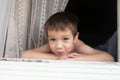 Portrait of happy little smiling boy kid is looking out of rustic wooden window and smiling. Summer time. Old rustic Royalty Free Stock Photo