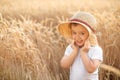 Portrait of happy little toddler boy in straw hat standing in wheat or rye field among golden spikes. Kid playing with hat outdoor