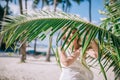 Portrait of happy long hair girl with amazing suntan wearing white dress near the nice green palm leave. Royalty Free Stock Photo