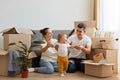 Portrait of happy loving couple with their baby kid moving in new flat, sitting on floor near cough and having fun with their Royalty Free Stock Photo