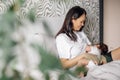 Portrait of happy loving mother breastfeeding her little daughter in bedroom, blurred foreground. Baby suckle milk and Royalty Free Stock Photo