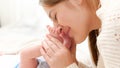 Portrait of happy loving mother kissing and holding little baby feet lying in crib. Concept of family happiness and Royalty Free Stock Photo