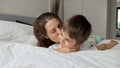 Portrait of happy loving mother lying on bed with her son in pajamas and kissing him. Concept of happy family, parents with kids, Royalty Free Stock Photo