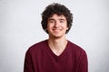 Portrait of happy male with broad smile, has curly hair, pleasant smile, dressed casually, stands against white background. Deligh