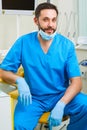 Portrait of happy male dentist wearing lab coat while sitting in clinic Royalty Free Stock Photo