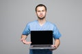 Portrait of a happy male doctor dressed in uniform with stethoscope showing blank screen laptop computer isolated over gray backgr Royalty Free Stock Photo