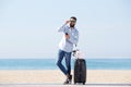 Portrait of happy man with suitcase and mobile phone standing on beach Royalty Free Stock Photo