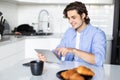 Portrait of happy man eat at breakfast and using digital tablet in kitchen at home Royalty Free Stock Photo