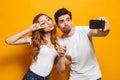 Portrait of happy man and woman taking selfie photo on smartphone and showing peace sign, isolated over yellow background Royalty Free Stock Photo