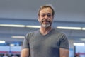 portrait of happy man 50-55 years old with beard in gray T-shirt on blurred background of railway station, vertical photo. Royalty Free Stock Photo