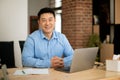 Portrait of happy mature asian man using laptop, sitting at table in living room and smiling at camera, free space Royalty Free Stock Photo