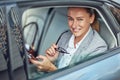 Portrait of a happy mature business woman sitting on back seat in the car and using smartphone, she is looking at camera Royalty Free Stock Photo