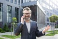 Portrait of happy mature businessman, gray haired man outside office building talking on the phone, boss smiling and